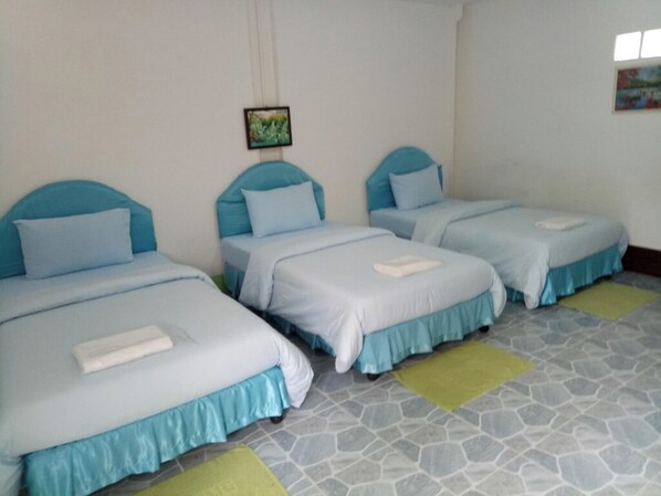 Habitación de hotel con tres camas individuales, cada una con cabecera azul y ropa de cama blanca. El piso tiene baldosas con un diseño geométrico.