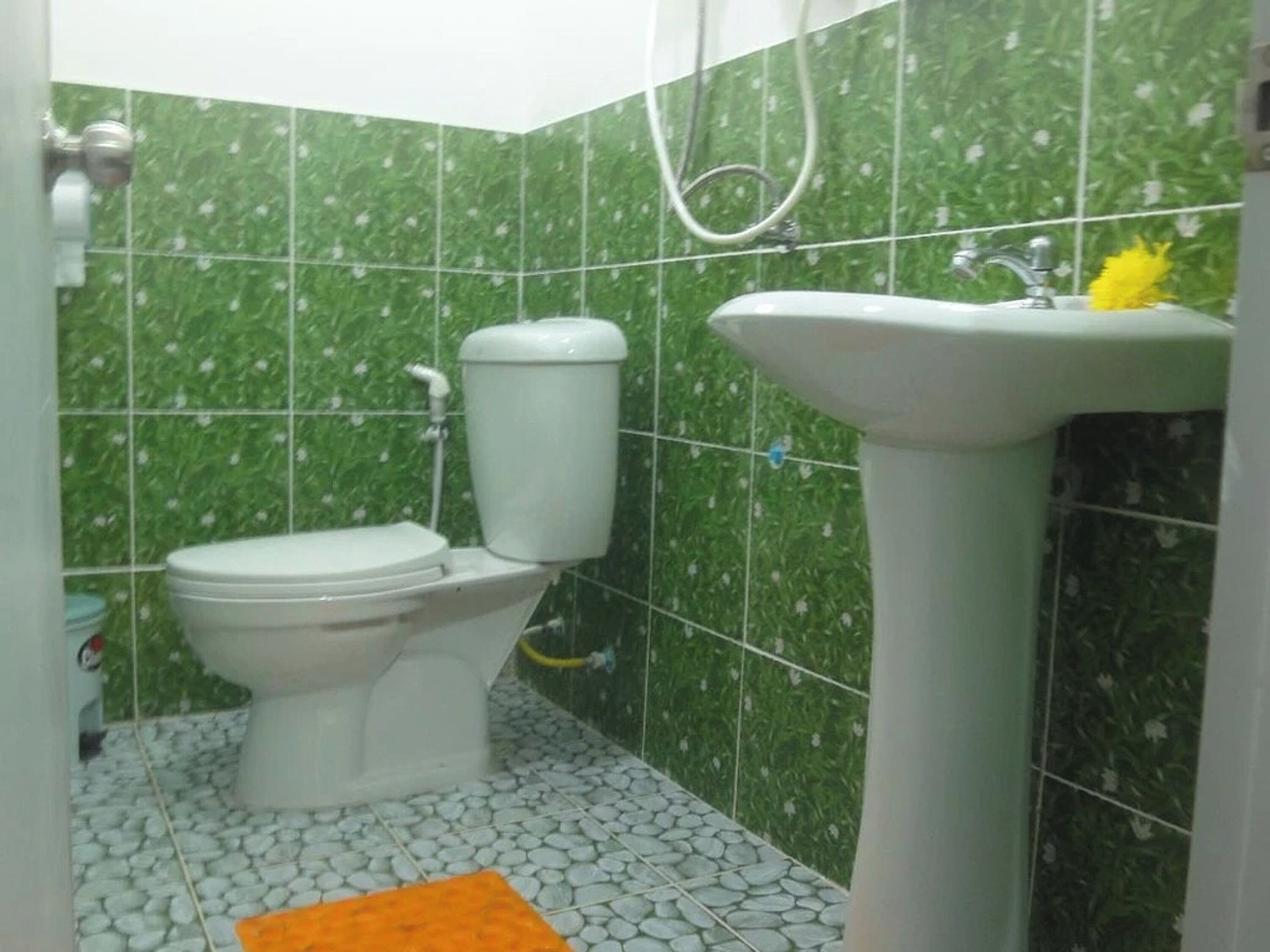 A bathroom with a toilet, sink, and green tiled walls.