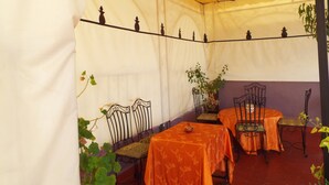 A covered outdoor seating area with tables and chairs, plants, and a decorative ceiling. - Maison Adam (Fes)