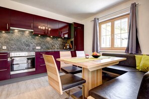 Una cocina moderna con armarios oscuros, horno empotrado y comedor con banco y mesa.