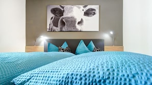 A bedroom with a bed, a headboard, and a wall-mounted picture of a cow. - Üser Schlössle Appartements (Brand)