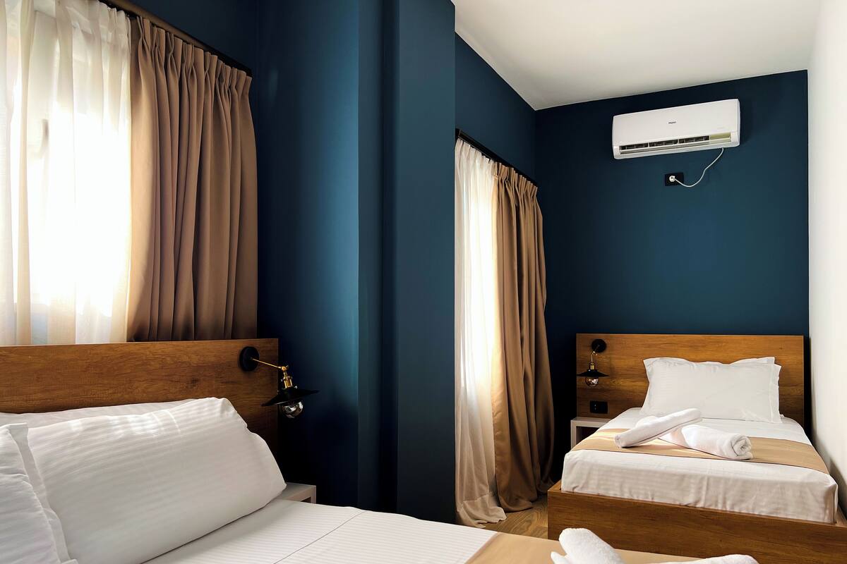 A hotel room with two beds, a wooden headboard, a wall-mounted air conditioner, and a window with curtains.