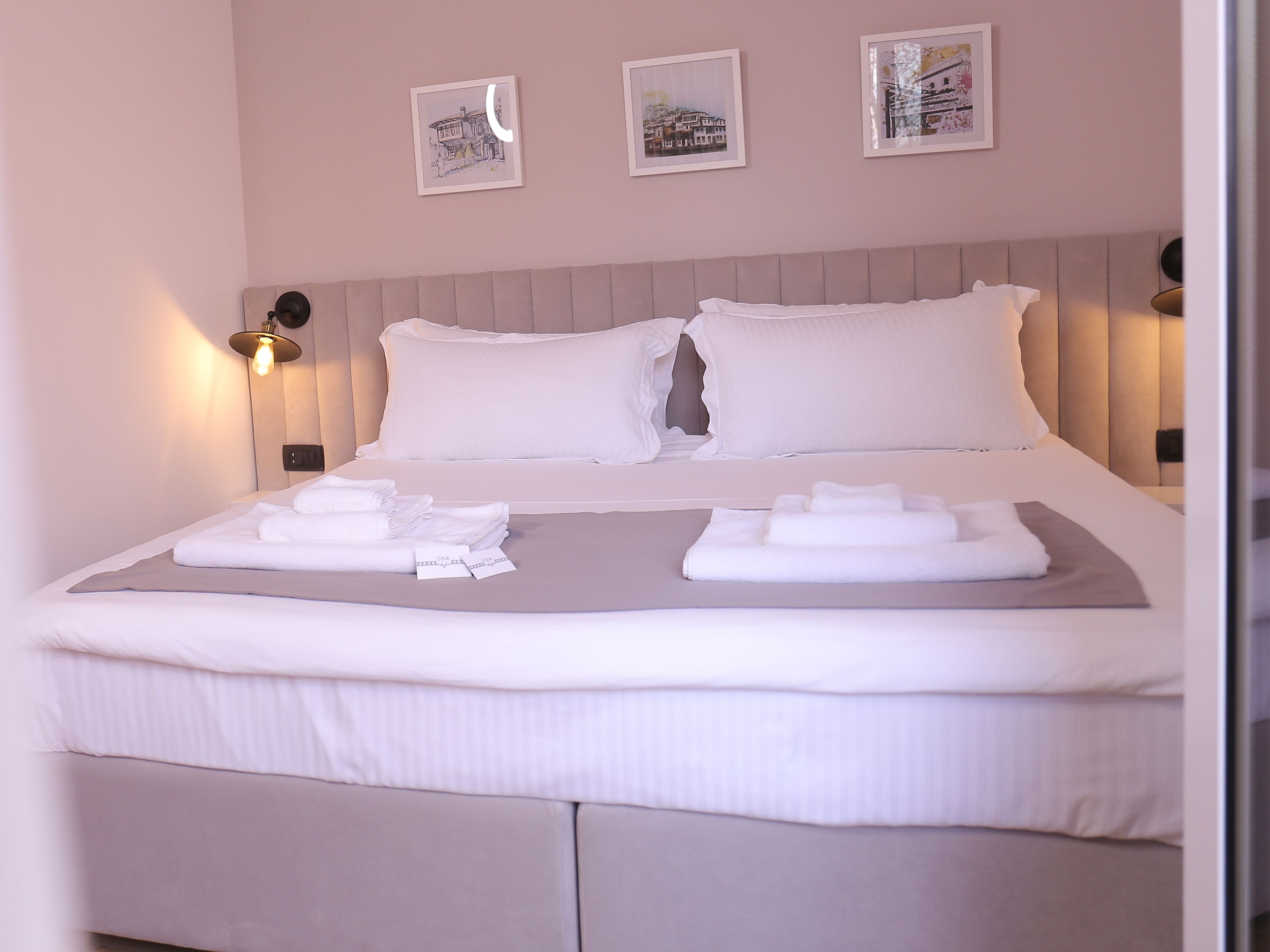 A neatly made bed with white linens and towels, a headboard with a light wood finish, and three framed pictures on the wall.