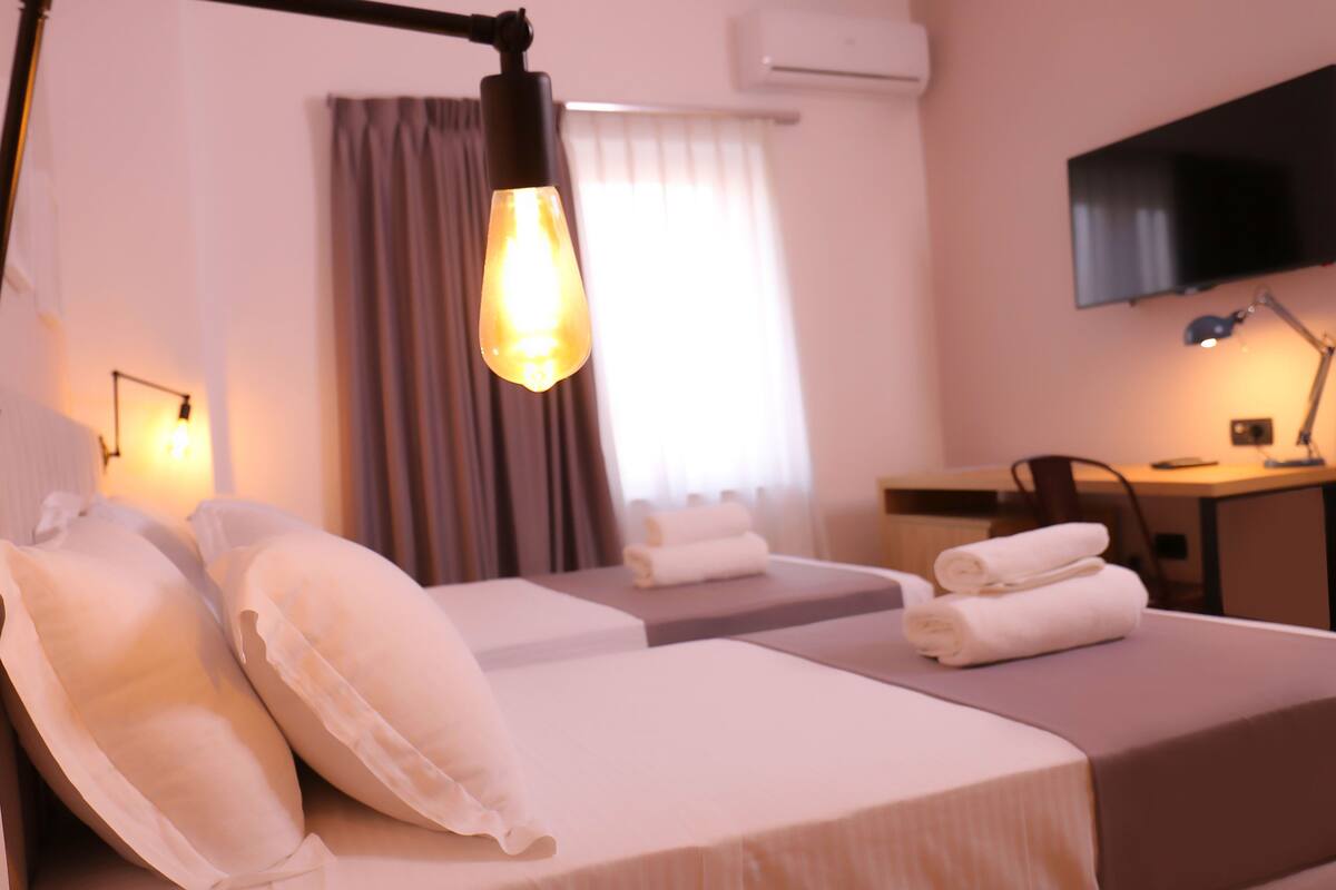 A hotel room with two beds, a desk, a chair, a TV, and a lamp.
