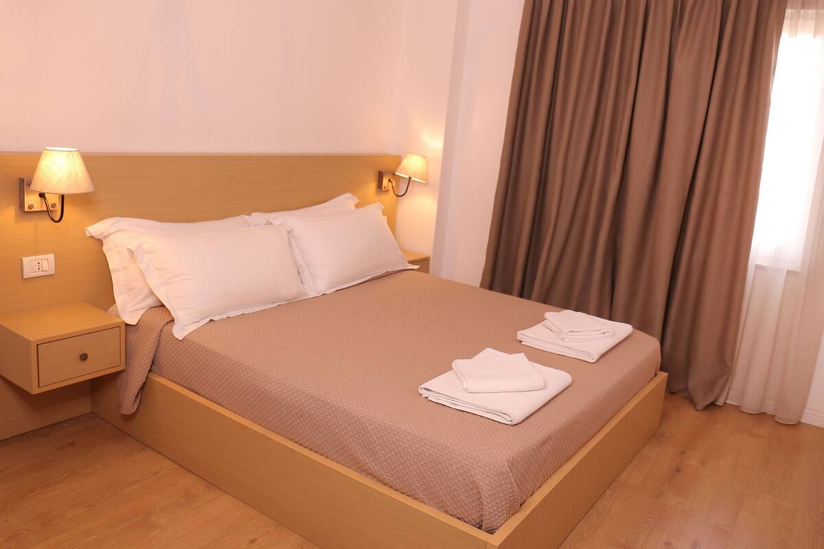 A neatly made bed with white linens, a wooden headboard, and two bedside lamps.
