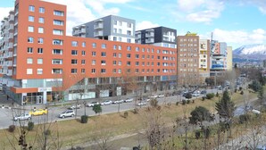 A multi-story hotel with a modern design, featuring a mix of red and grey facades, large windows, and a parking area with several cars. - Oda Hotel Tirana (Tirana)