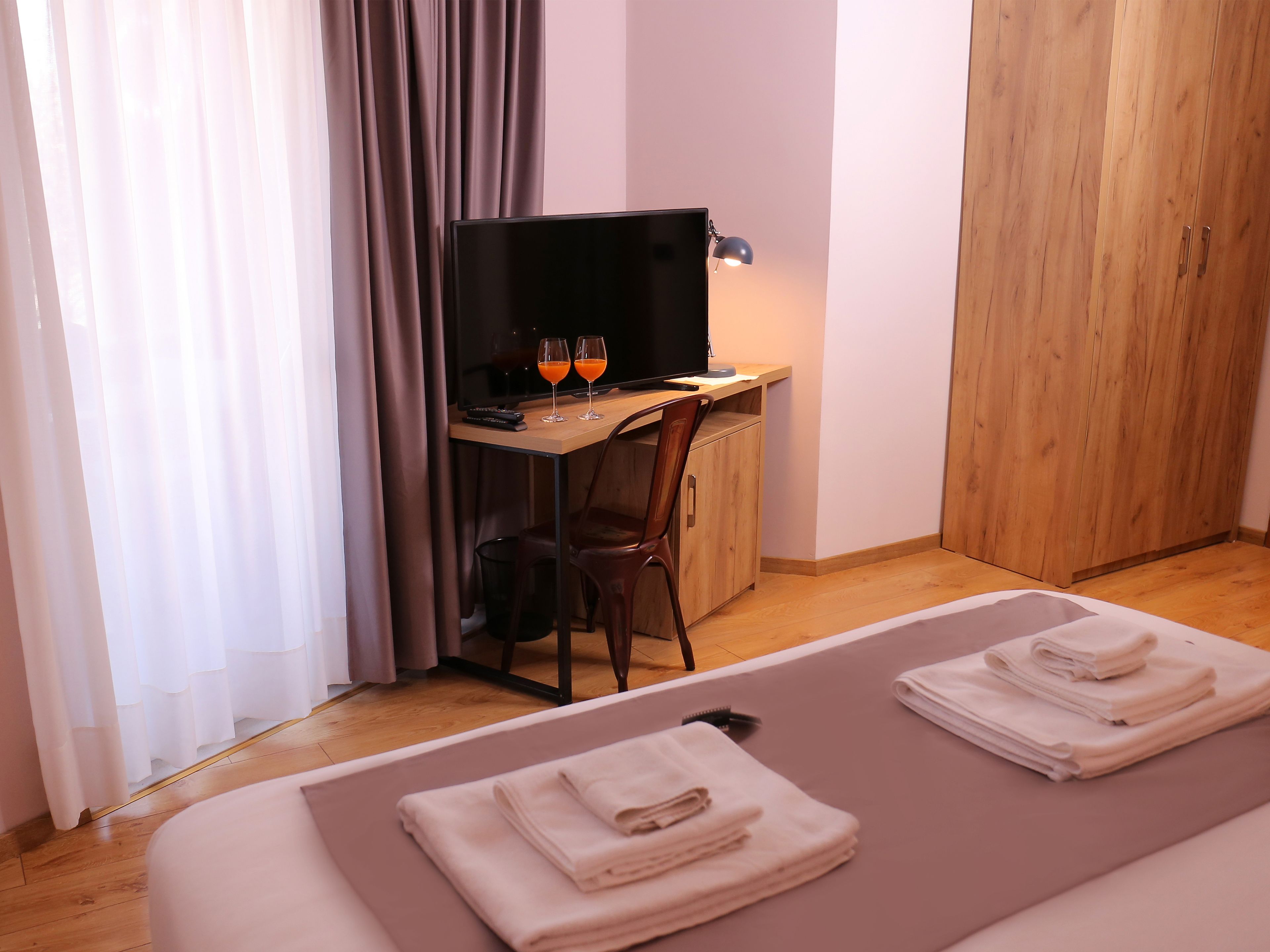 Hotellihuone, jossa on sänky, työpöytä tietokoneella, kaksi lasillista appelsiinimehua ja lamppu.