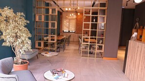 A modern interior with a dining area, a reception desk, and a seating area with a potted plant. - Oda Hotel Tirana (Tirana)