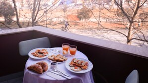 A table with breakfast items, including croissants, toast, and fruit, set on a balcony with a view of buildings and trees. - Oda Hotel Tirana (Tirana)