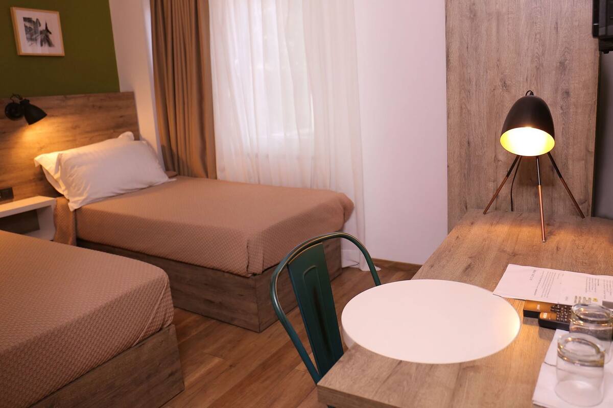 A hotel room with two beds, a wooden headboard, a desk with a lamp, a chair, and a table with a menu.