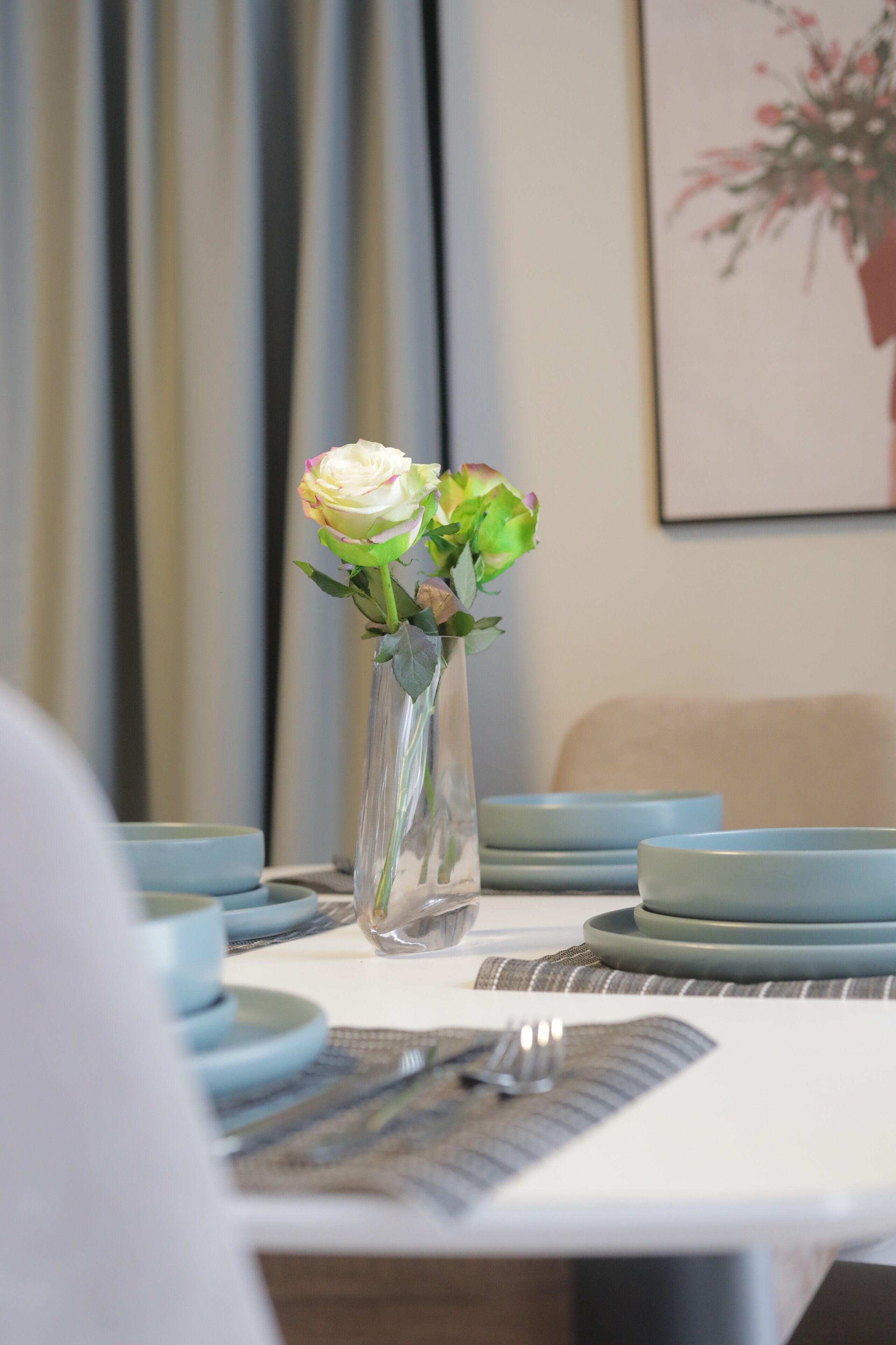 A dining table with a vase of flowers, blue plates, and a fork on a placemat.