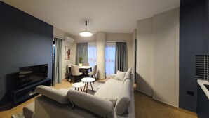 A modern living room with a sofa, a TV, a dining table with chairs, and a small coffee table. - Oda Hotel Tirana (Tirana)