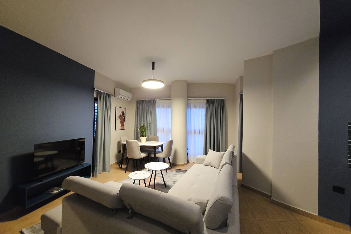 A modern living room with a sofa, a TV, a dining table with chairs, and a small coffee table.
