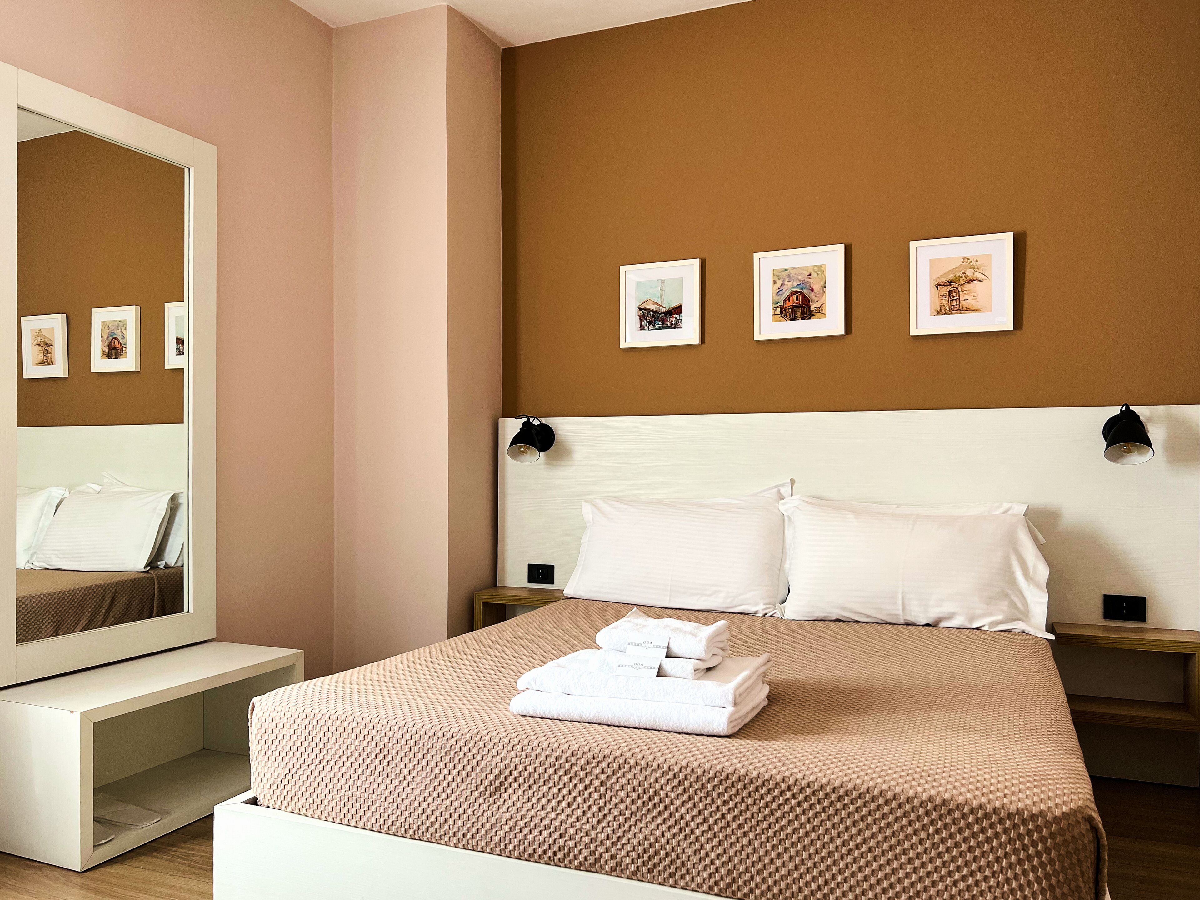 Ein ordentlich eingerichtetes Hotelzimmer mit einem großen Bett, einem Nachttisch, einem Spiegel und drei gerahmten Bildern an der Wand.