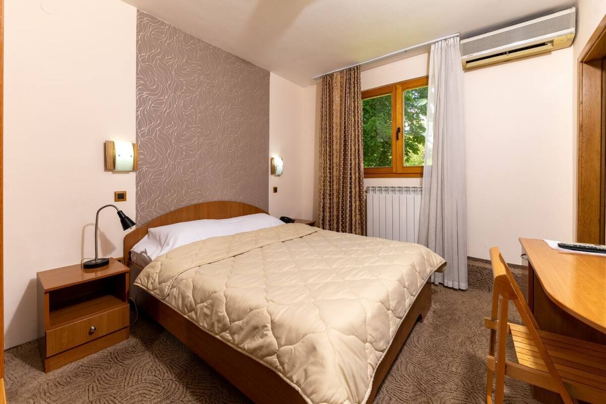 A neatly arranged hotel room with a bed, bedside table, lamp, and a desk with a chair.