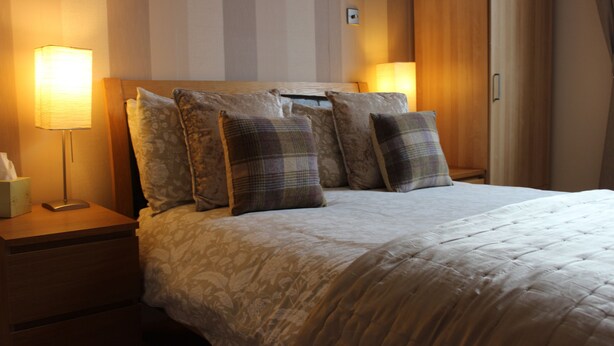 A neatly made bed with a floral-patterned duvet, a wooden headboard, and multiple decorative pillows. - Valhalla B&B (Alexandria)