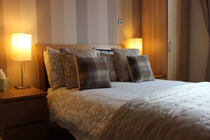 A neatly made bed with a floral-patterned duvet, a wooden headboard, and multiple decorative pillows. - Valhalla B&B (Alexandria)