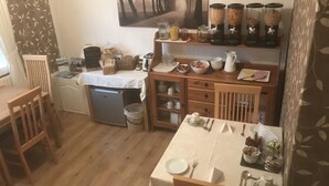 A compact kitchen with a refrigerator, a sink, and a dining area with a table set for two. There are shelves with jars and a painting on the wall. - Valhalla B&B (Alexandria)