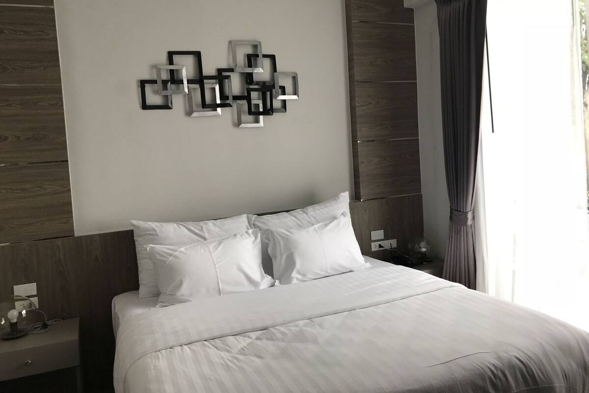 A modern hotel room with a large bed, a wall-mounted abstract art piece, and a nightstand with a lamp.