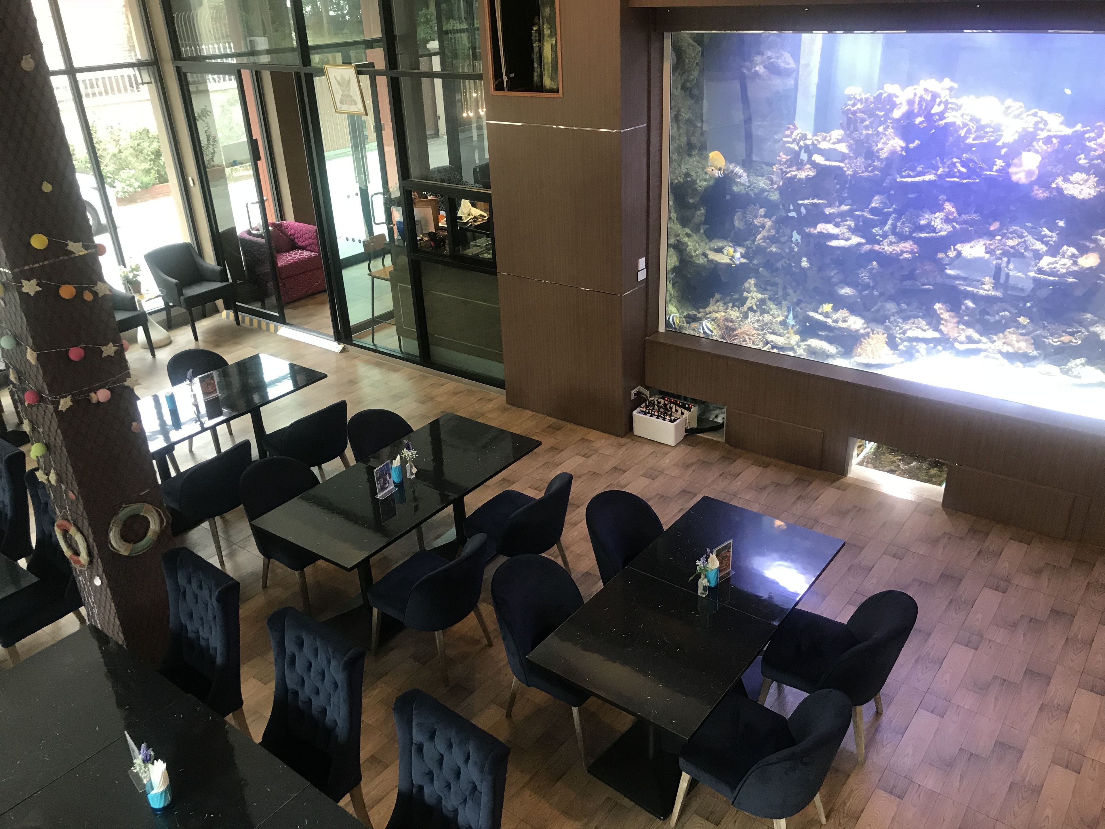 Een restaurant met tafels en stoelen, een groot aquarium en uitzicht op de omgeving.
