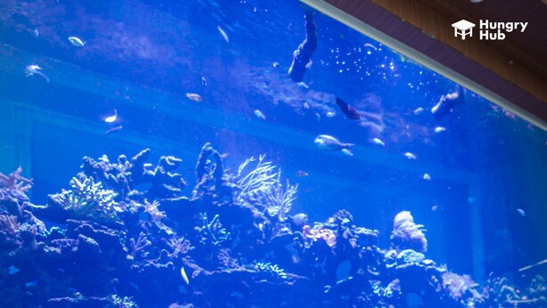 A dining area with a large aquarium in the background, a pizza, and various dishes on the table.