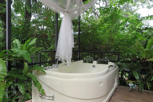 A white hot tub with a transparent canopy, surrounded by lush greenery and a metal railing.