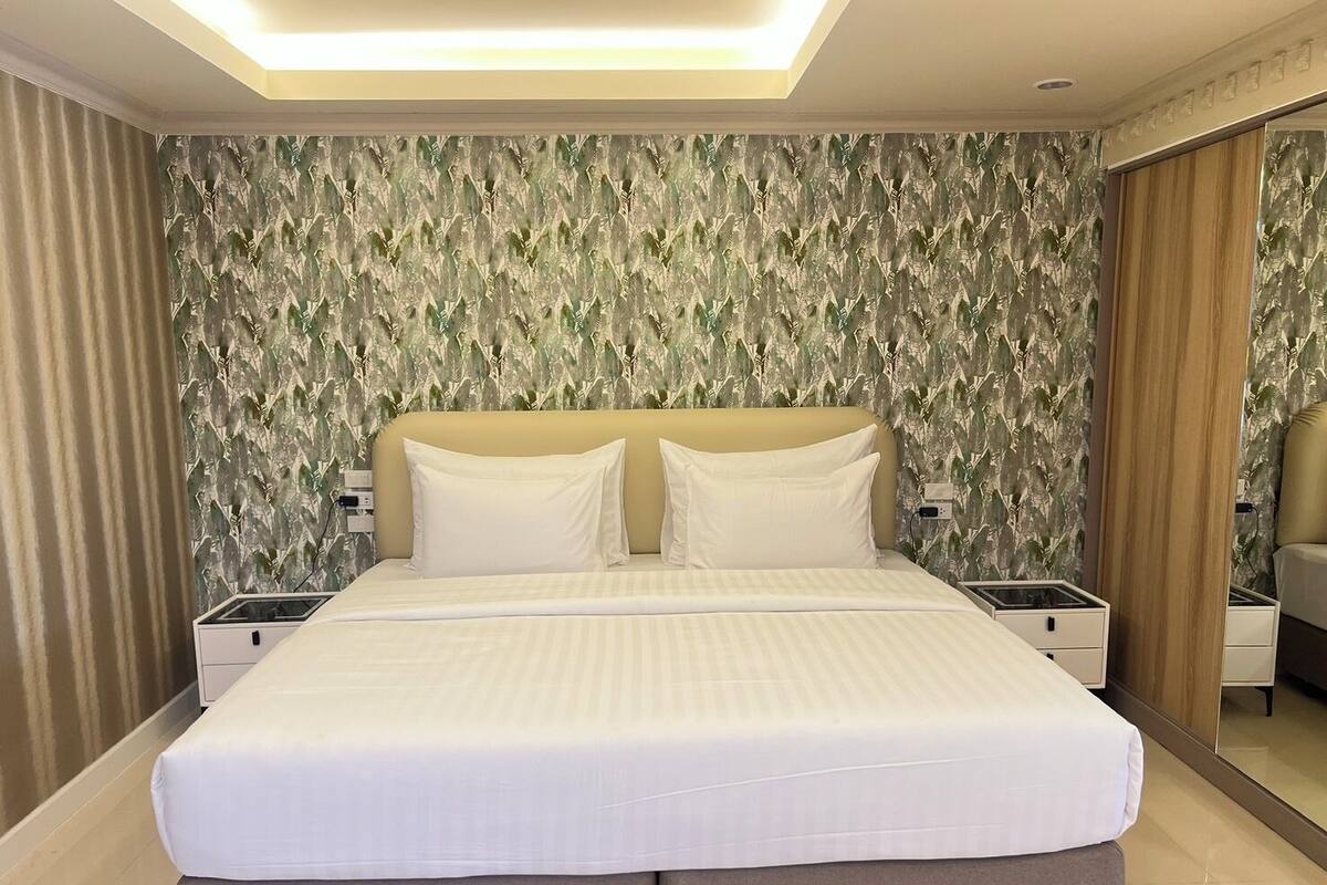 A modern hotel room with a large bed, two bedside tables, and a mirror.