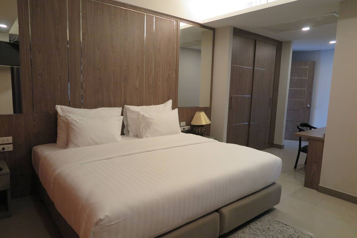 A modern bedroom with a large bed, wooden wardrobe, and a mirror.