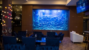 A modern lounge with a large aquarium, comfortable seating, and a television screen.