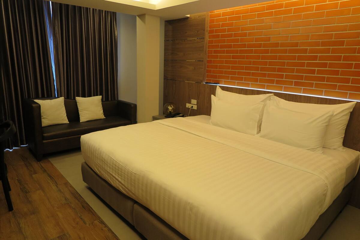 A hotel room with a large bed, a sofa, a nightstand, and a brick accent wall.