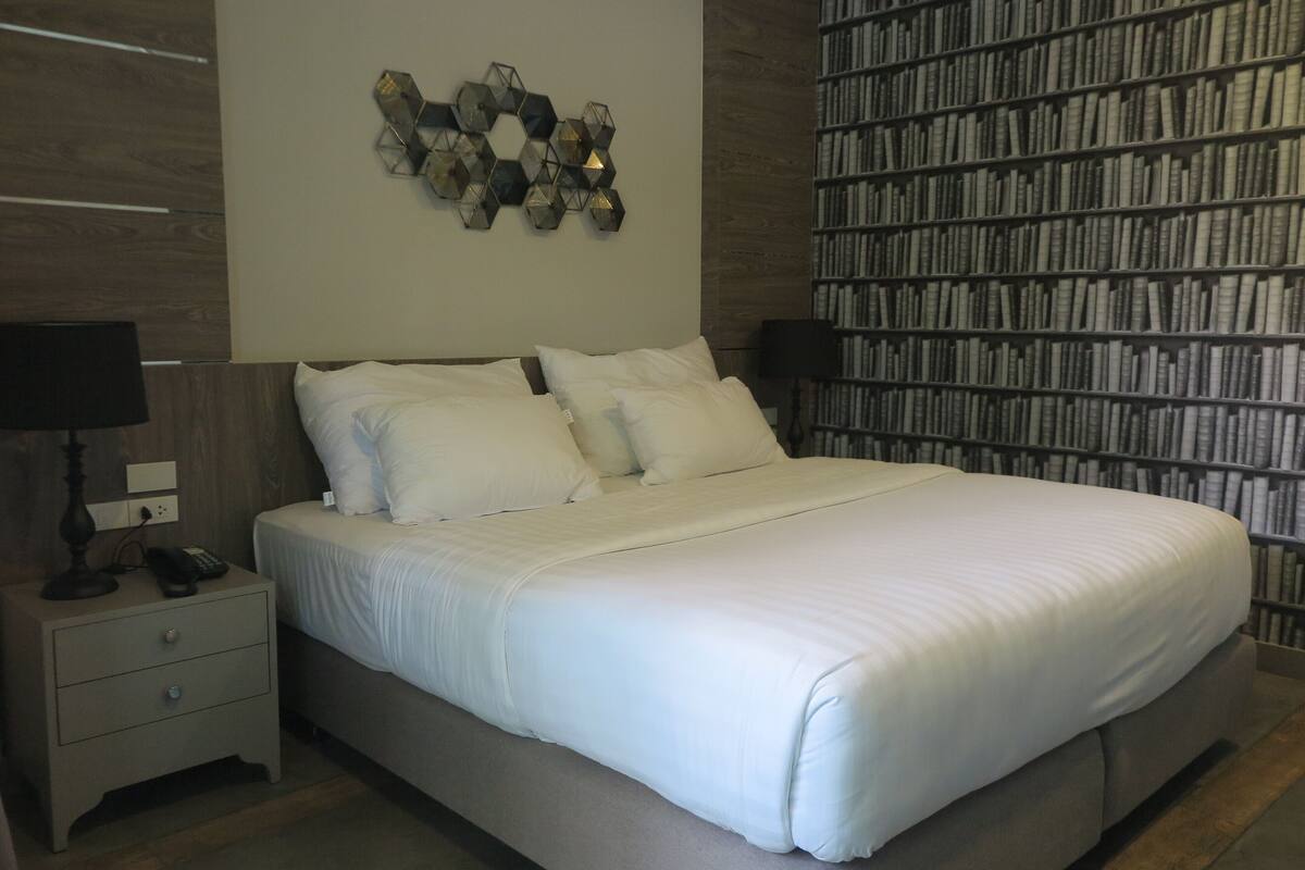 A neatly made bed with white linens, a bedside table with a lamp, and a wall-mounted geometric decoration.