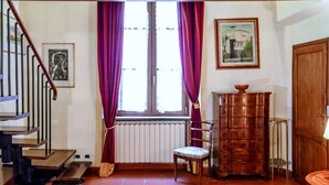 Una escalera con barandilla de madera, una ventana con cortinas moradas, un radiador, un mueble de madera y un cuadro en la pared.