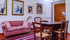 Una sala de estar con un sofá rosa, una mesa de comedor de madera y sillas, obras de arte enmarcadas en las paredes y una puerta de madera.