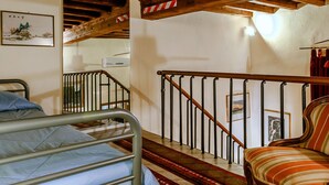 Una habitación con una cama, una silla, una escalera y una pared decorada con cuadros.
