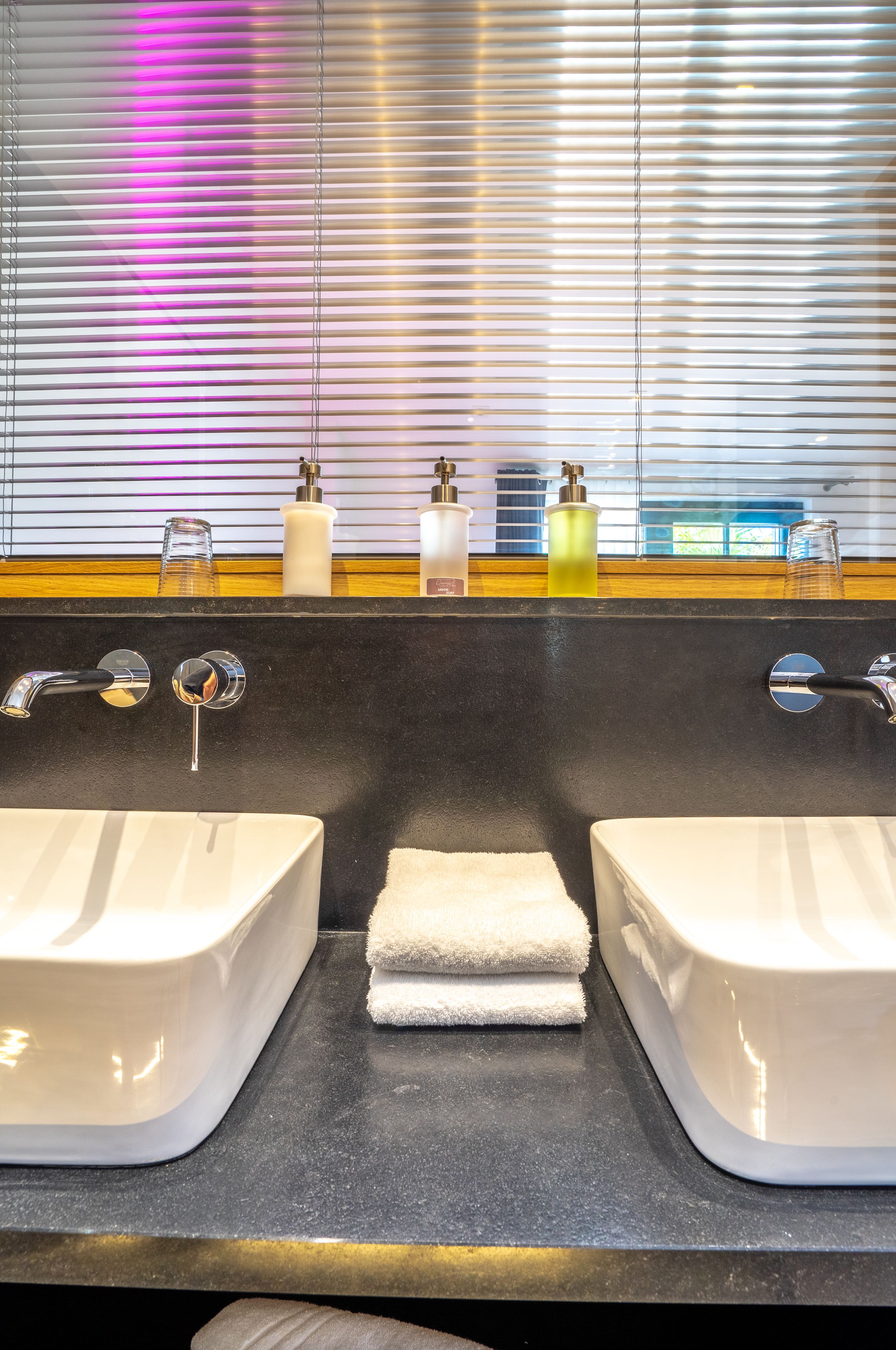A bathroom with two sinks, a mirror, and a window with blinds.