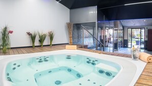 A modern indoor pool area with a hot tub, wooden flooring, and glass doors leading to an outdoor patio. - Hôtel Ile de Ré (Le Bois-Plage-en-Re)