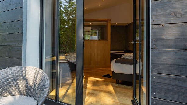 A modern interior with a glass door leading to a bedroom, a wicker chair outside, and a wooden deck. - Hôtel Ile de Ré (Le Bois-Plage-en-Re)