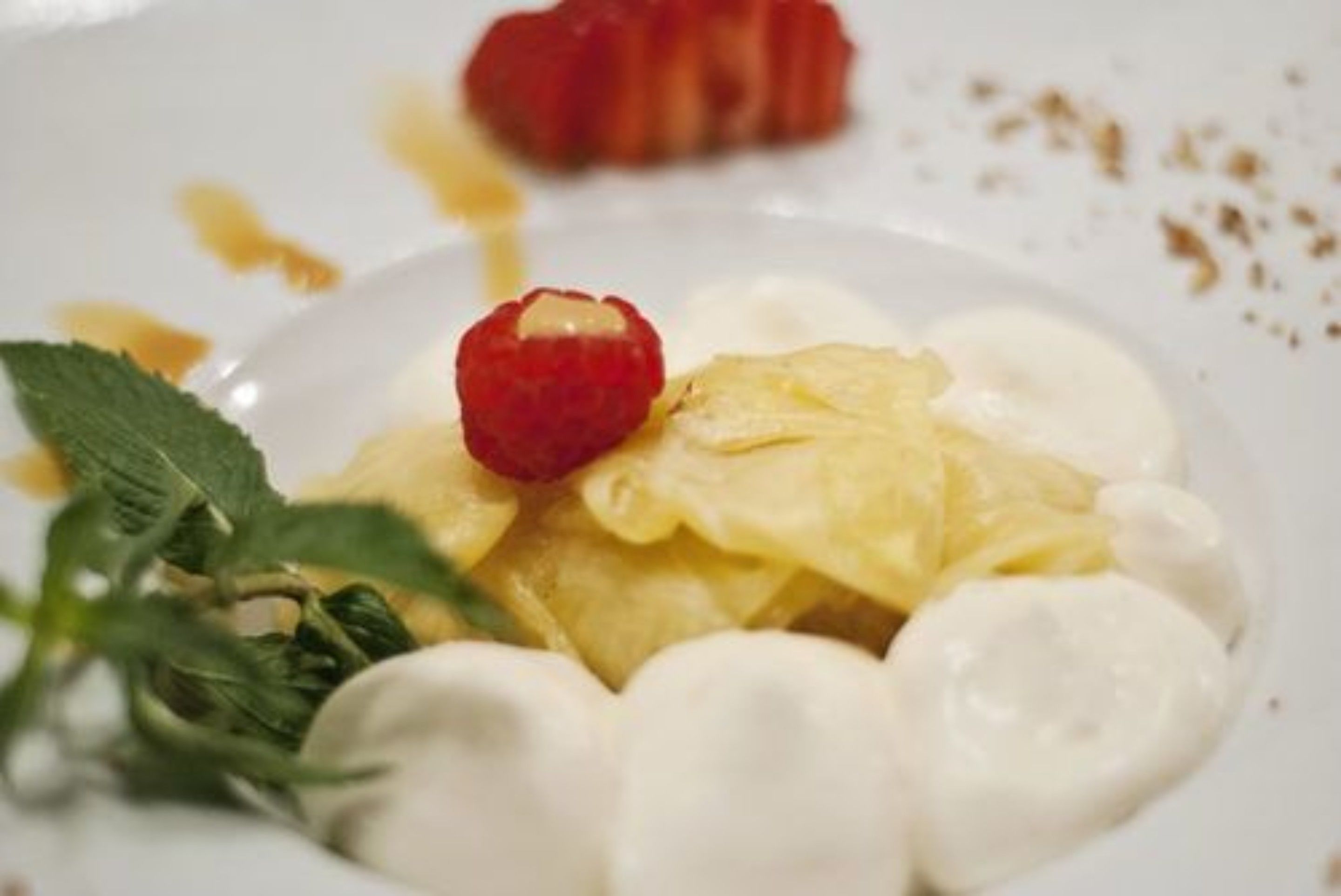 Un plato de postre con frambuesa, crema y una hoja decorativa.