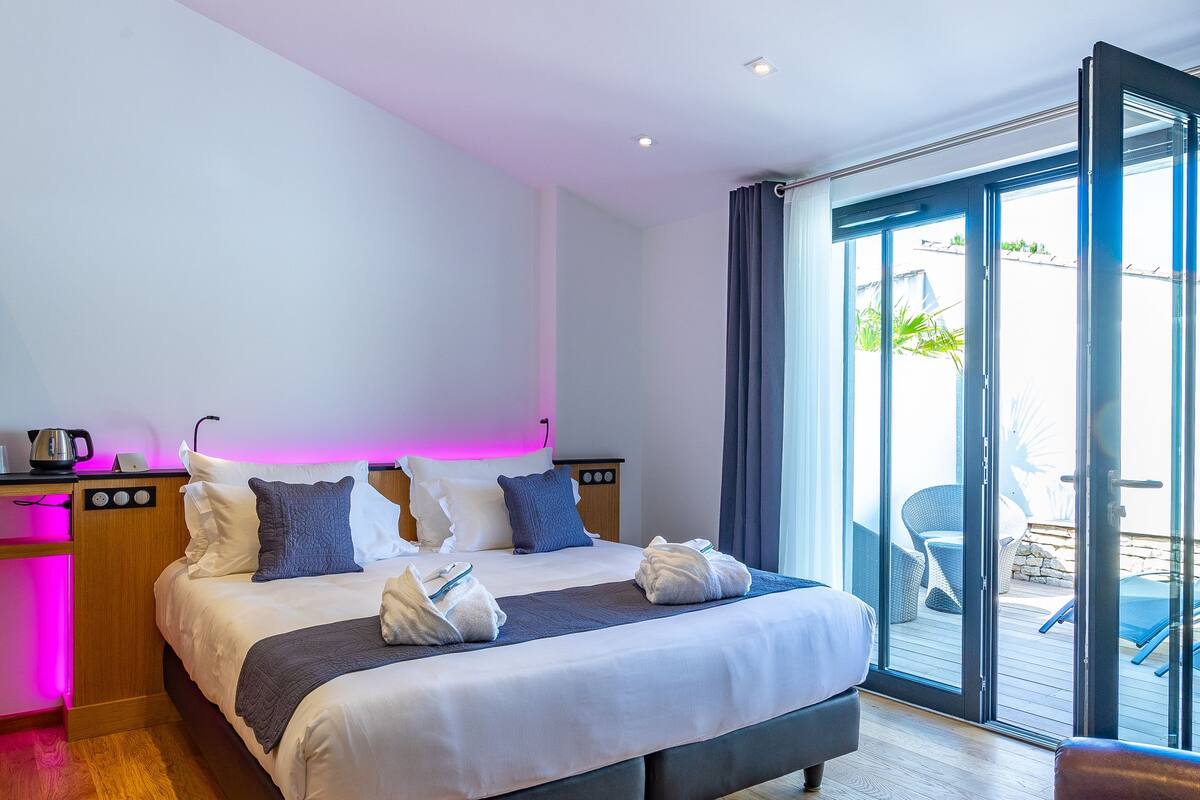 Habitación de hotel moderna con una cama grande, piso de madera y vista a un área exterior a través de un ventanal.
