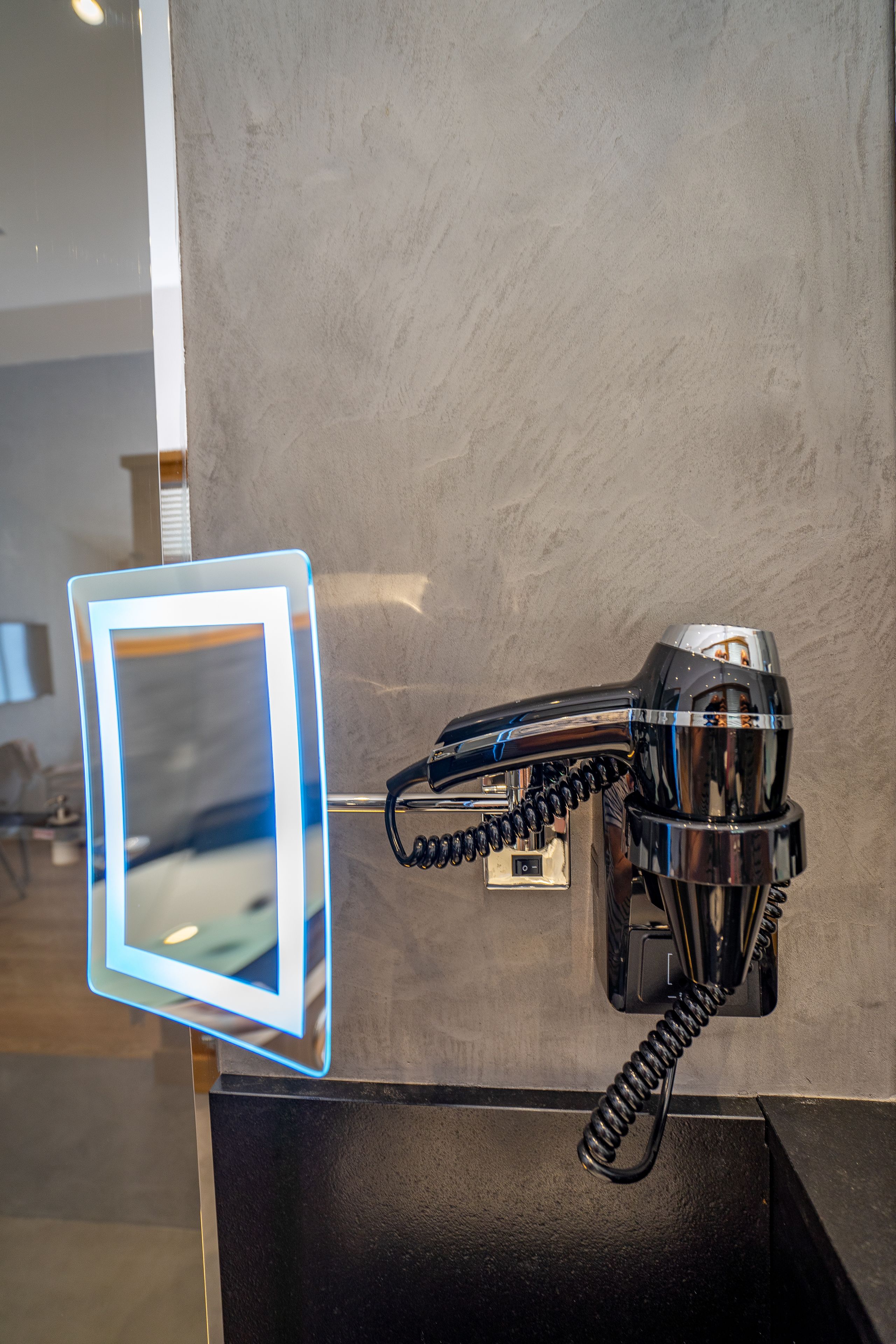 A hairdryer mounted on a wall with a mirror and phone.