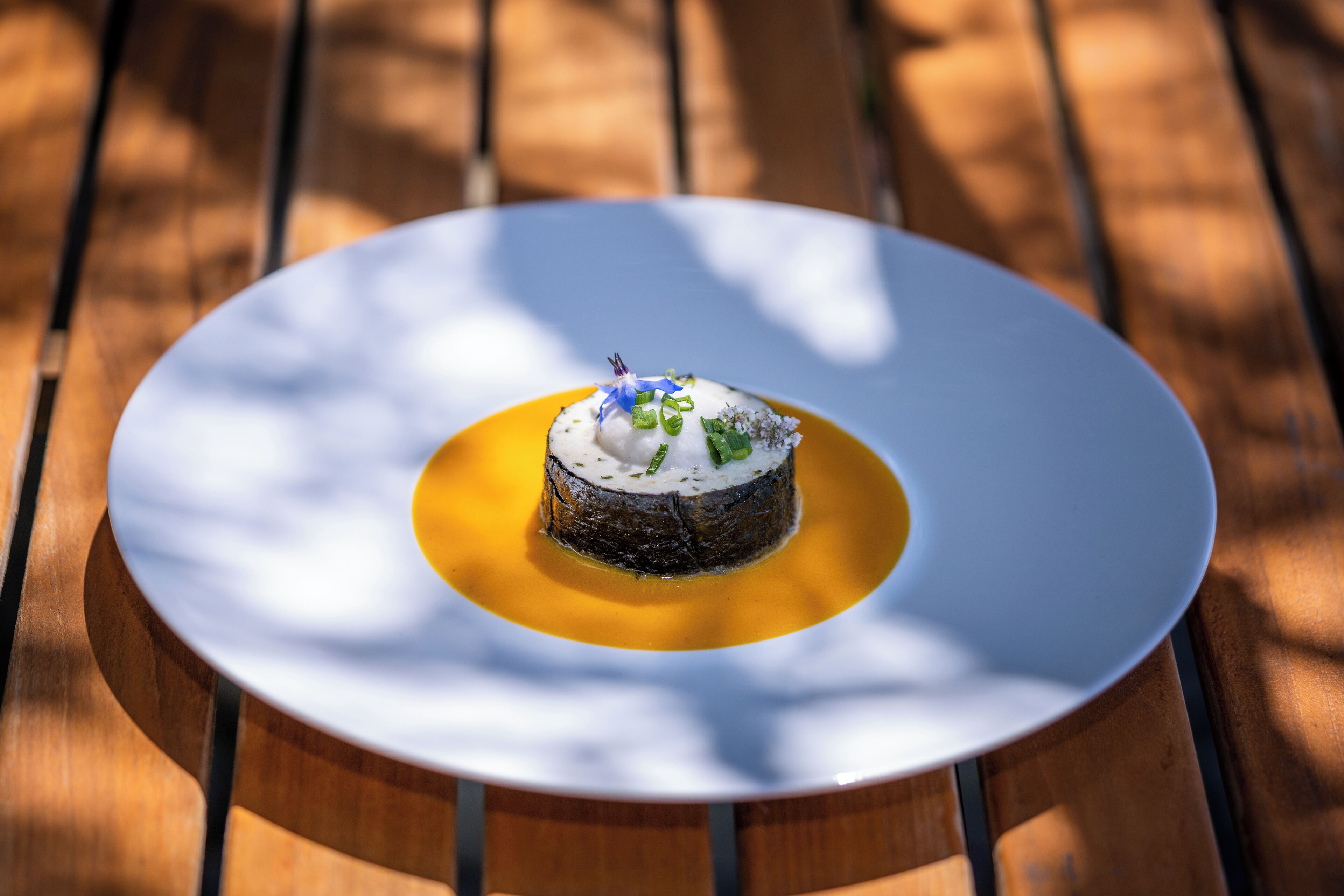 Un postre en un plato blanco con salsa amarilla, sobre una mesa de madera.