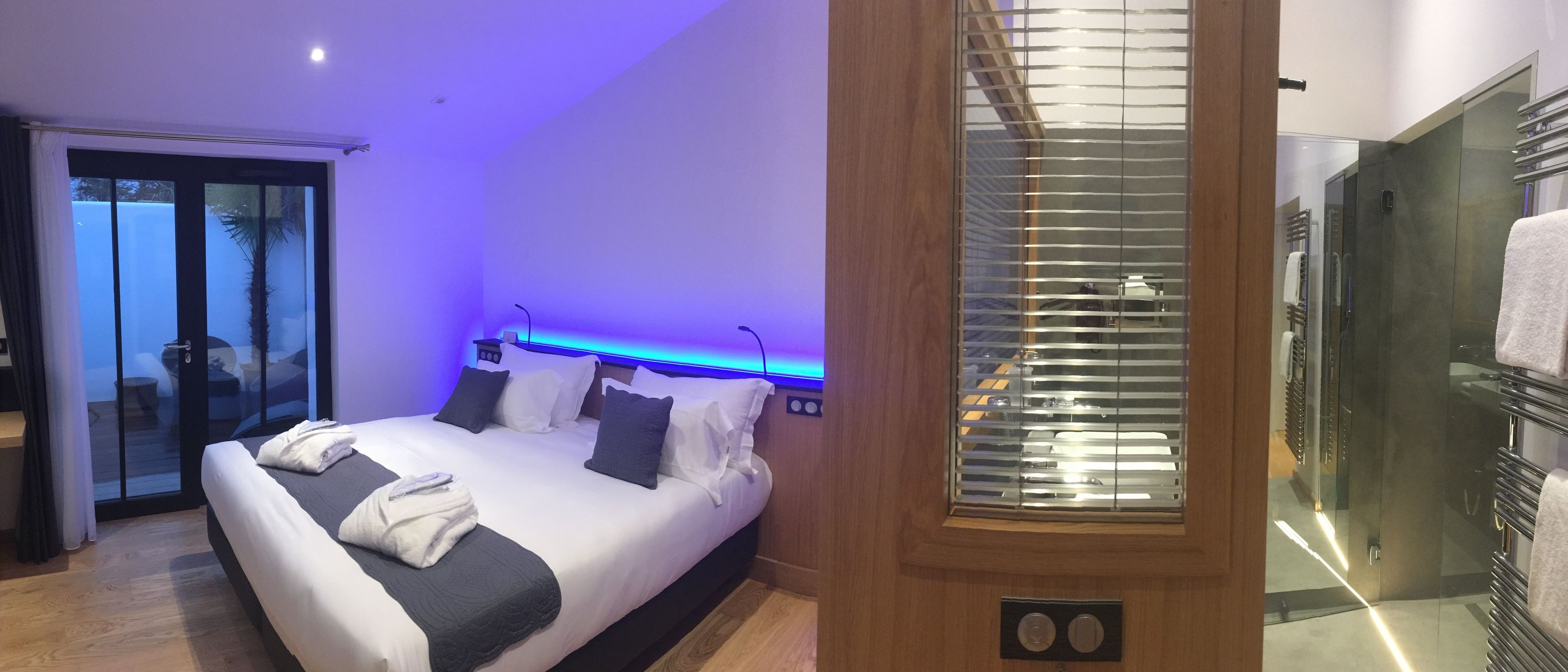 A modern hotel room with a large bed, a glass door leading to a balcony, and a shower area with a glass enclosure.