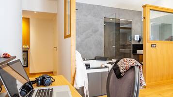 Une chambre d’hôtel moderne avec un bureau en bois, un ordinateur portable, une tasse de café et une assiette contenant une pâtisserie.