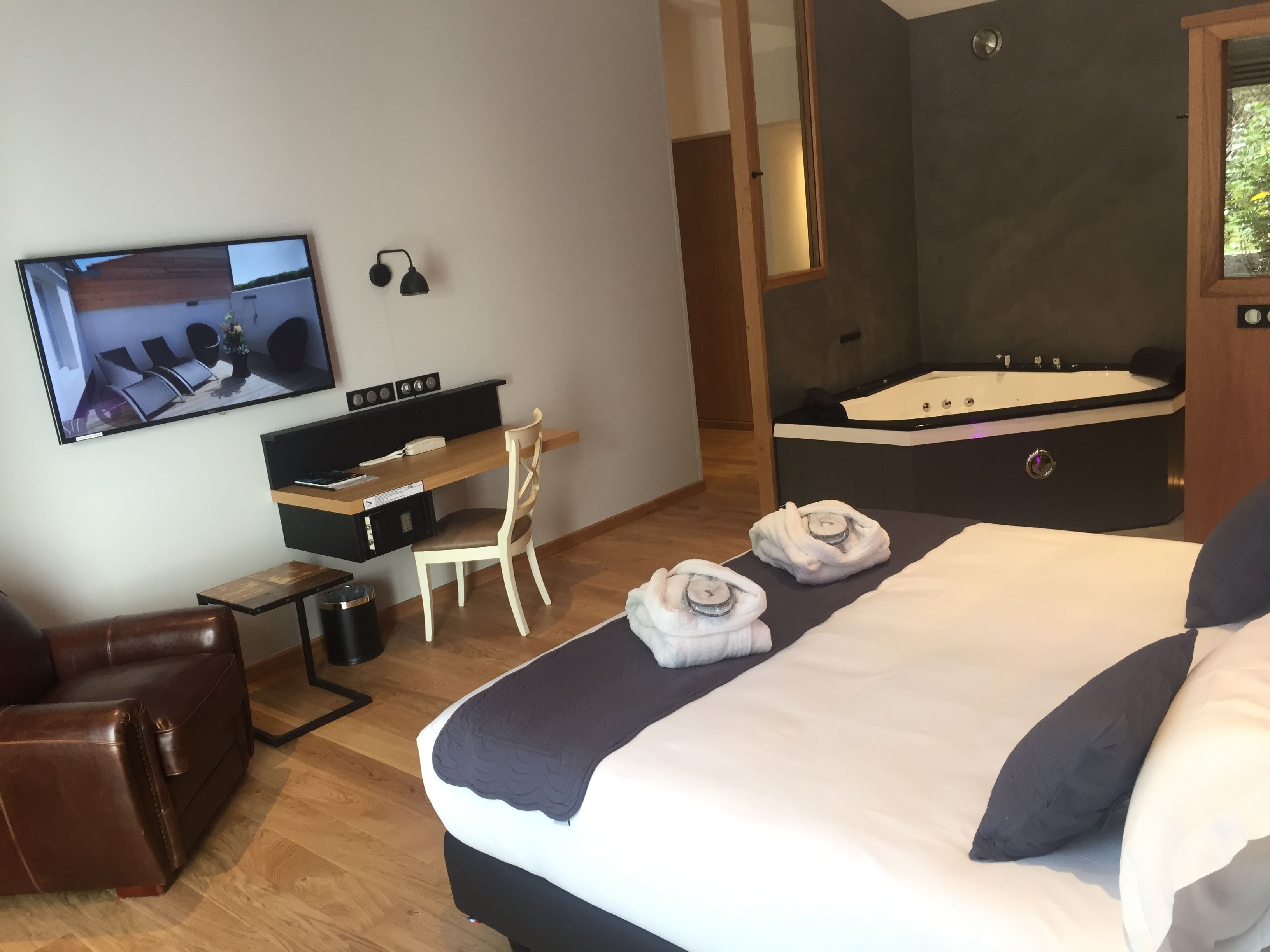 A hotel room with a bed, a desk, a chair, a TV, and a jacuzzi.
