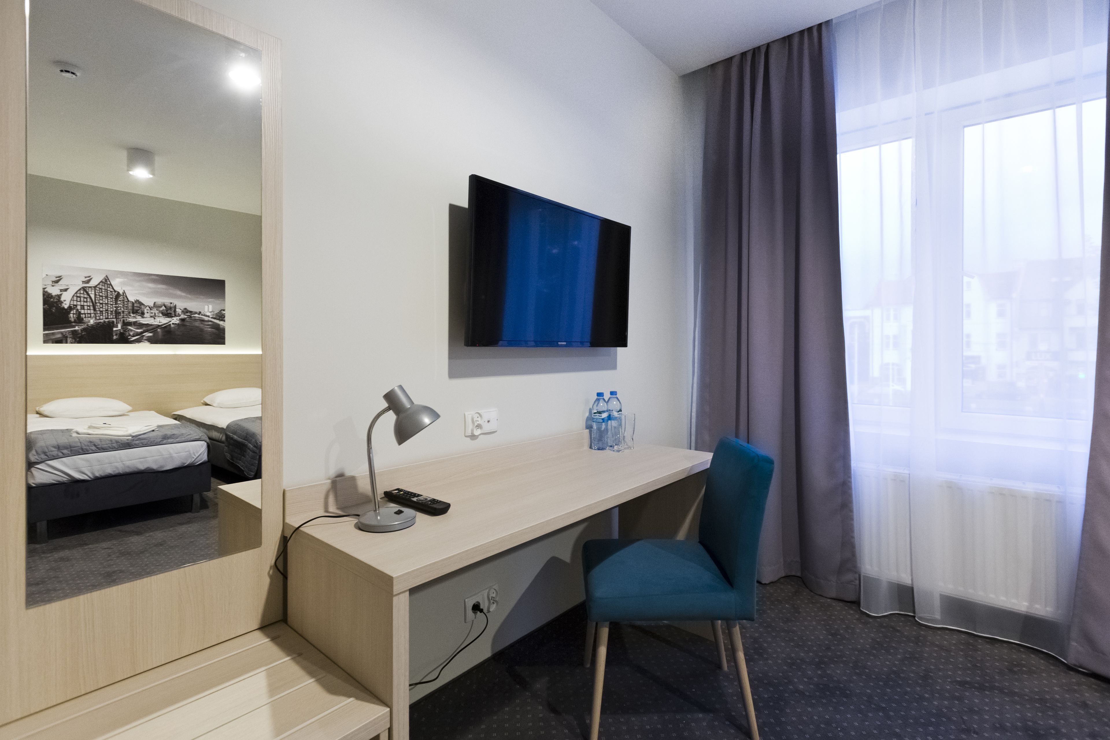 Hotelkamer met een bed, bureau met lamp, stoel, televisie en raam met gordijnen.