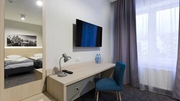 A hotel room with a bed, a desk with a lamp, a chair, a TV, and a window with curtains.