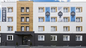 Un moderno edificio de hotel con estructura de dos plantas, que presenta una combinación de fachadas blancas y de madera, numerosas ventanas y señalización destacada del hotel.