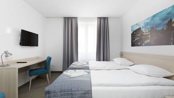 A hotel room with a bed, a desk, a chair, a TV, and a painting on the wall.