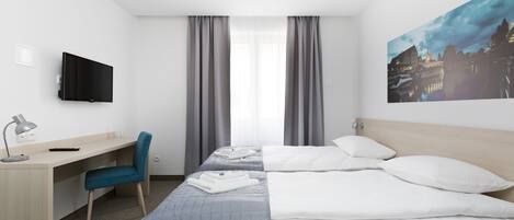 Una habitación de hotel con una cama, un escritorio, una silla, un televisor y un cuadro en la pared.