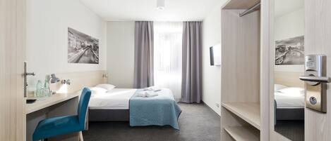 Una habitación de hotel con cama, escritorio con silla, armario y espejo de baño.